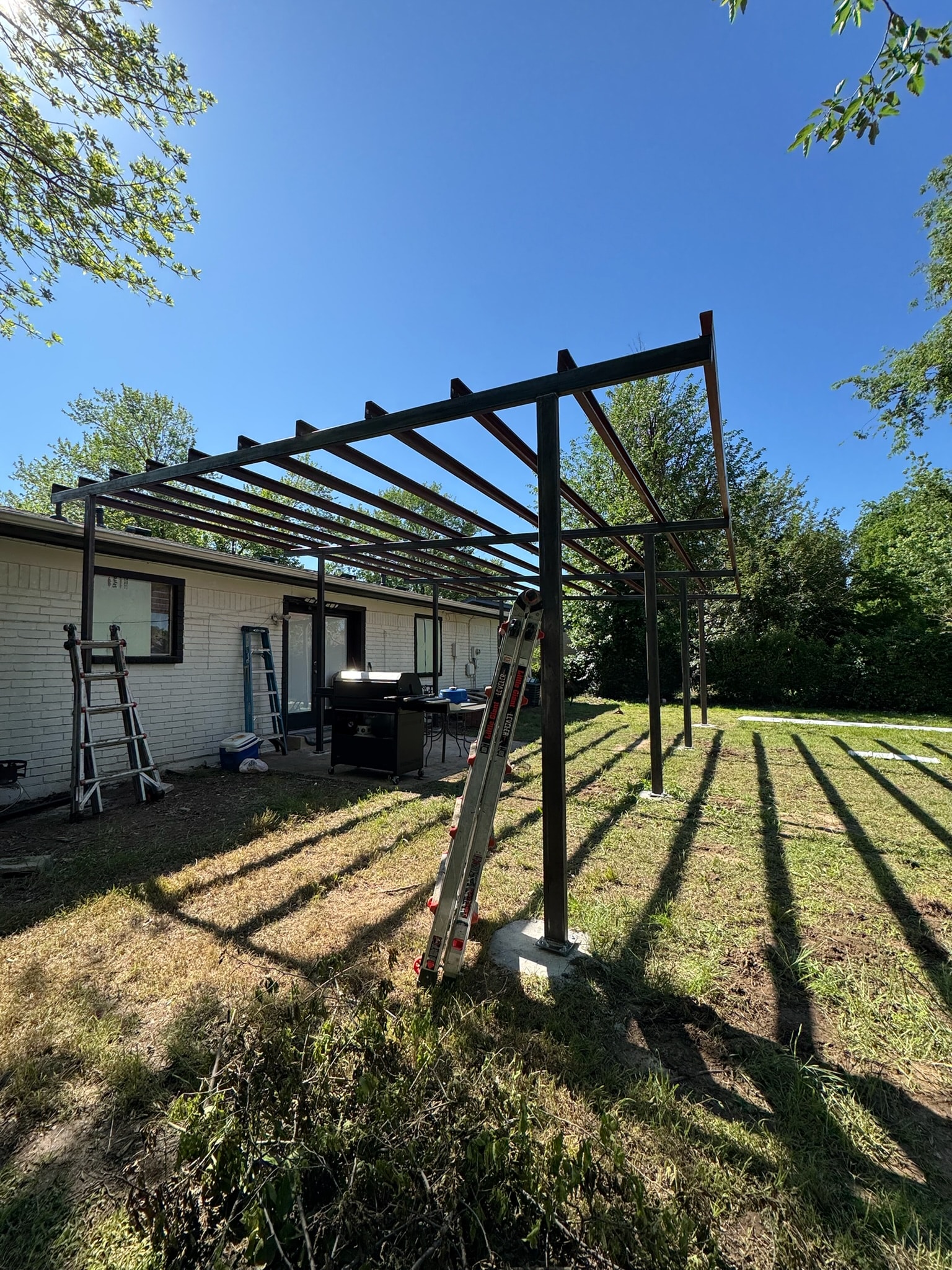 Backyard patio cover frame under construction beside a white brick home