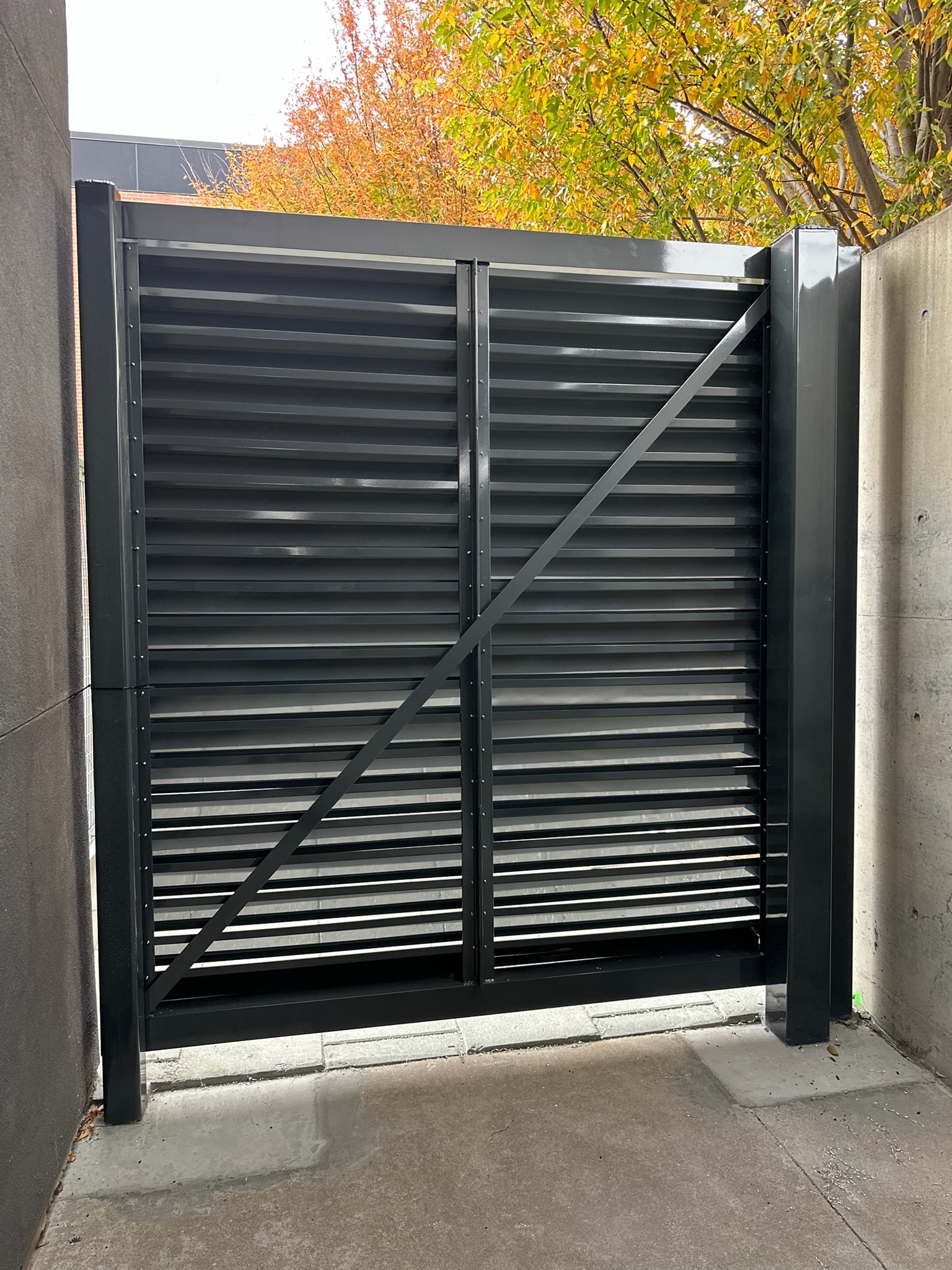 Modern black slatted steel privacy gate installed between concrete walls