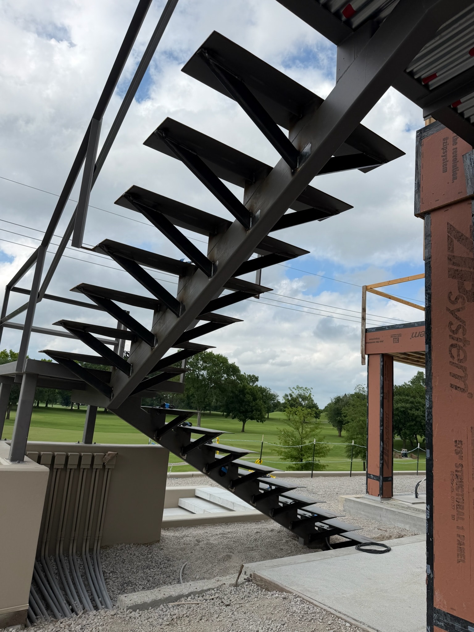 Custom black steel staircase under construction beside a golf course