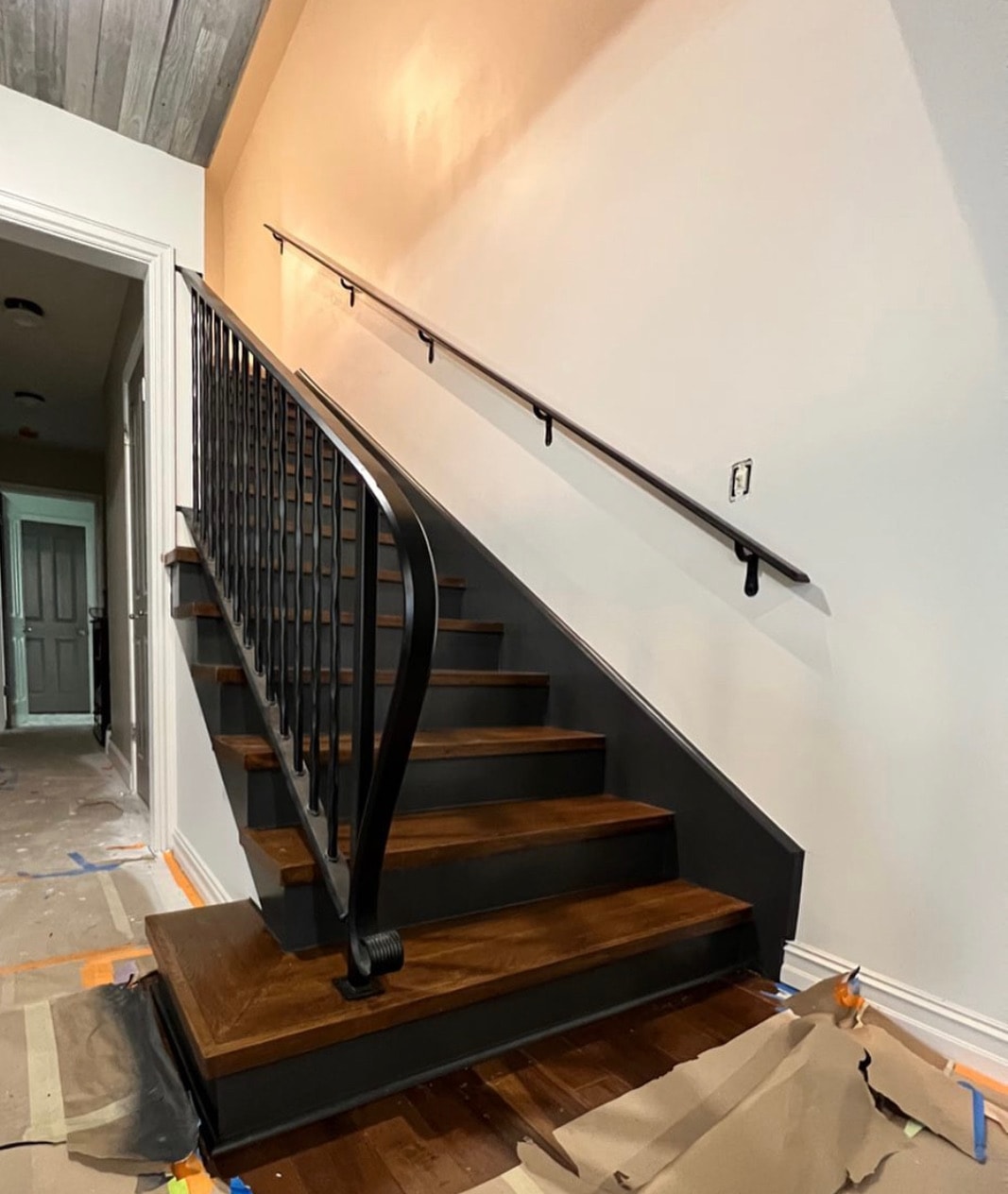Custom black steel stair railing and wall-mounted handrail installed in a residential interior