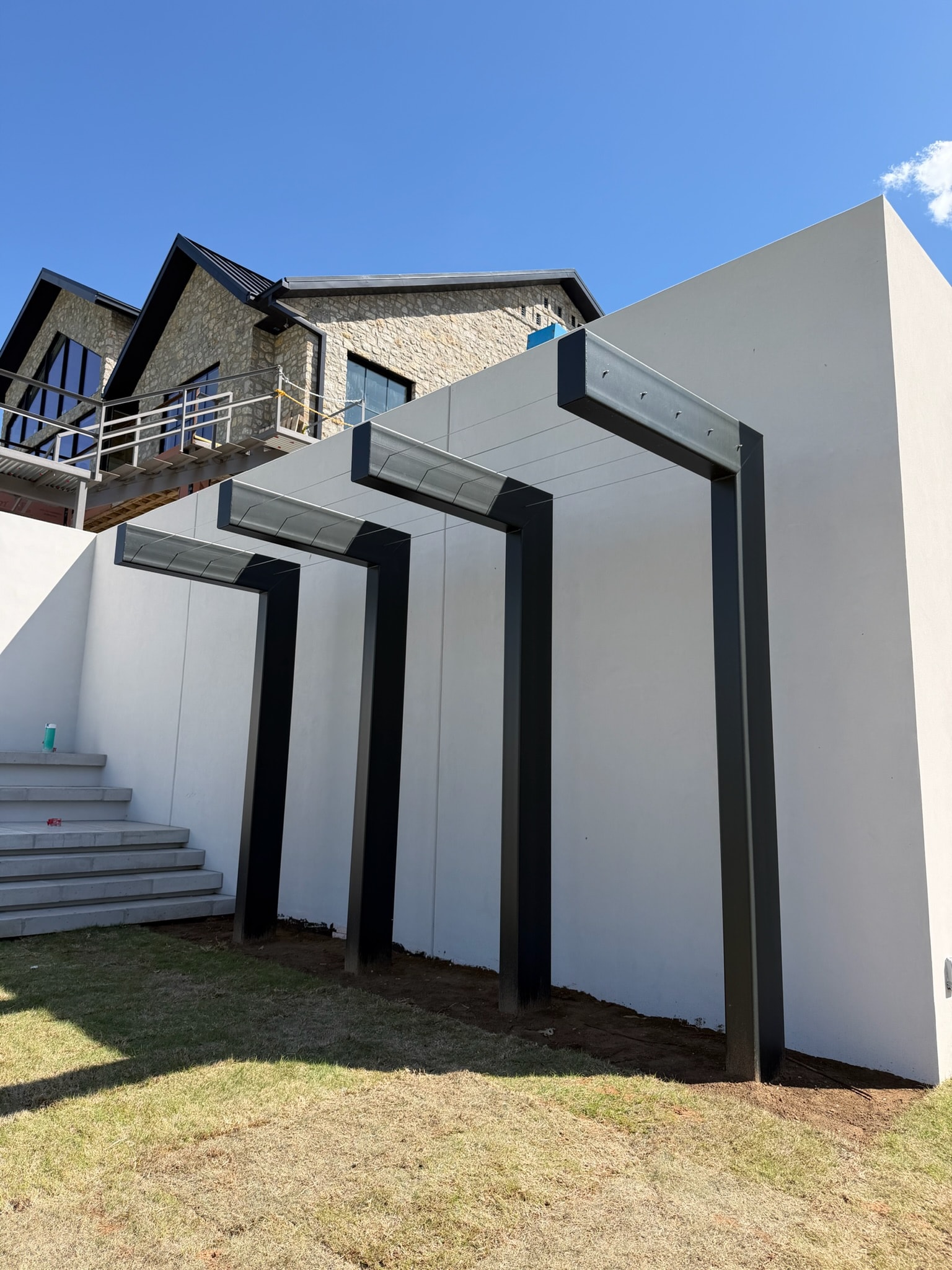 Custom black steel pergola framing beside a modern residence