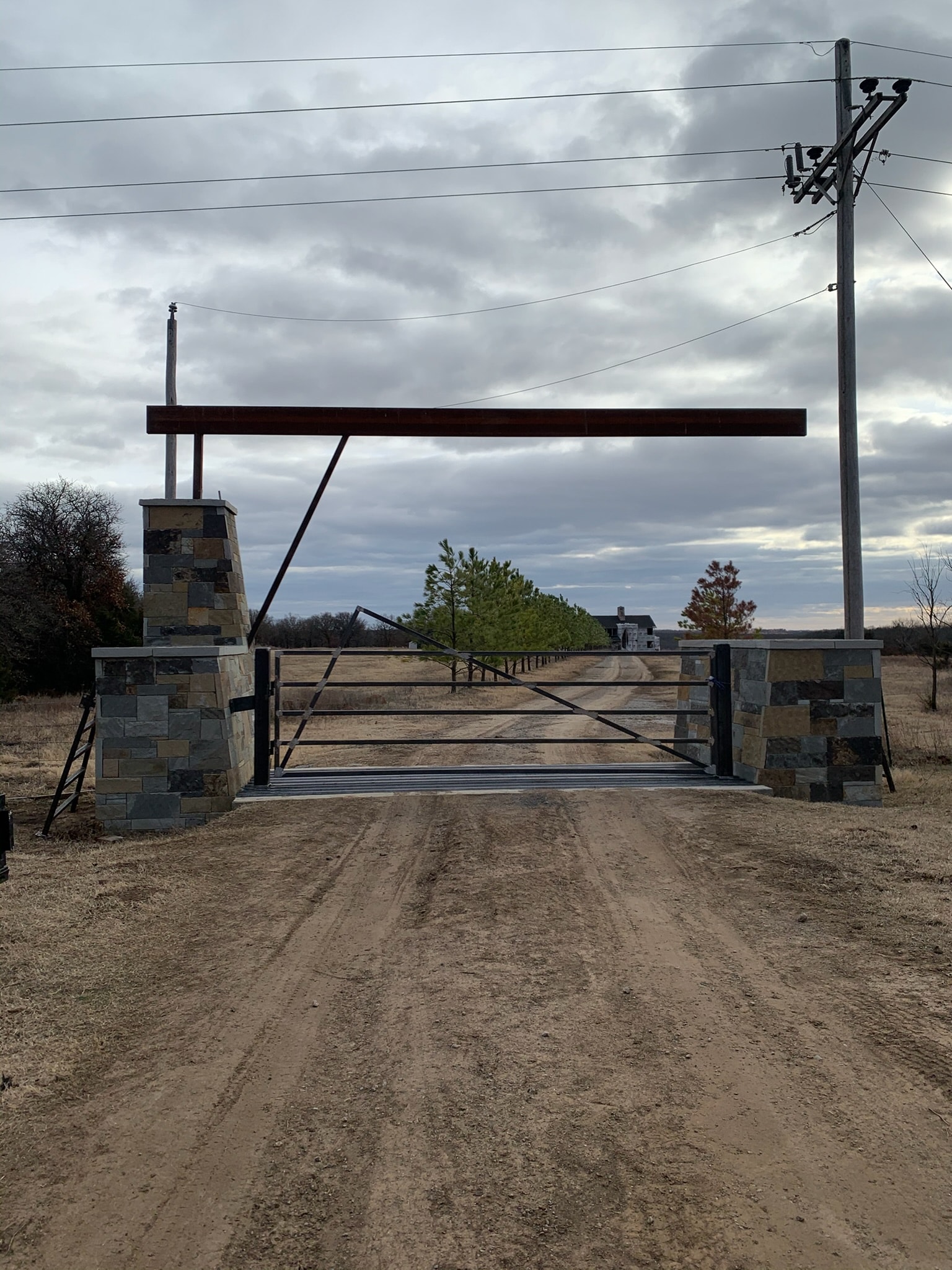 Custom steel ranch gate installed between stone entrance columns