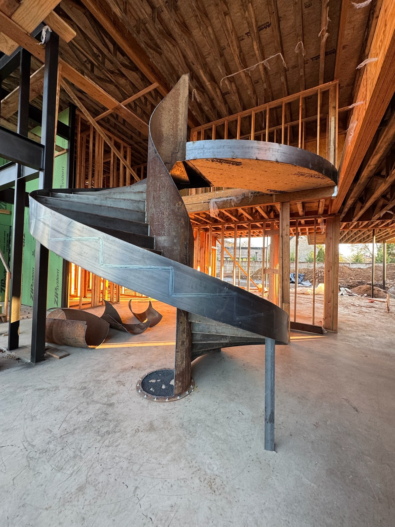 Custom sculptural steel spiral staircase under construction inside a framed home